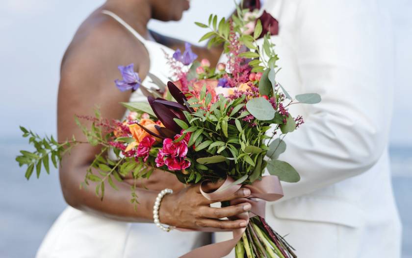 Black couple holding beautiful bouquet of flowers while embracing on wedding day